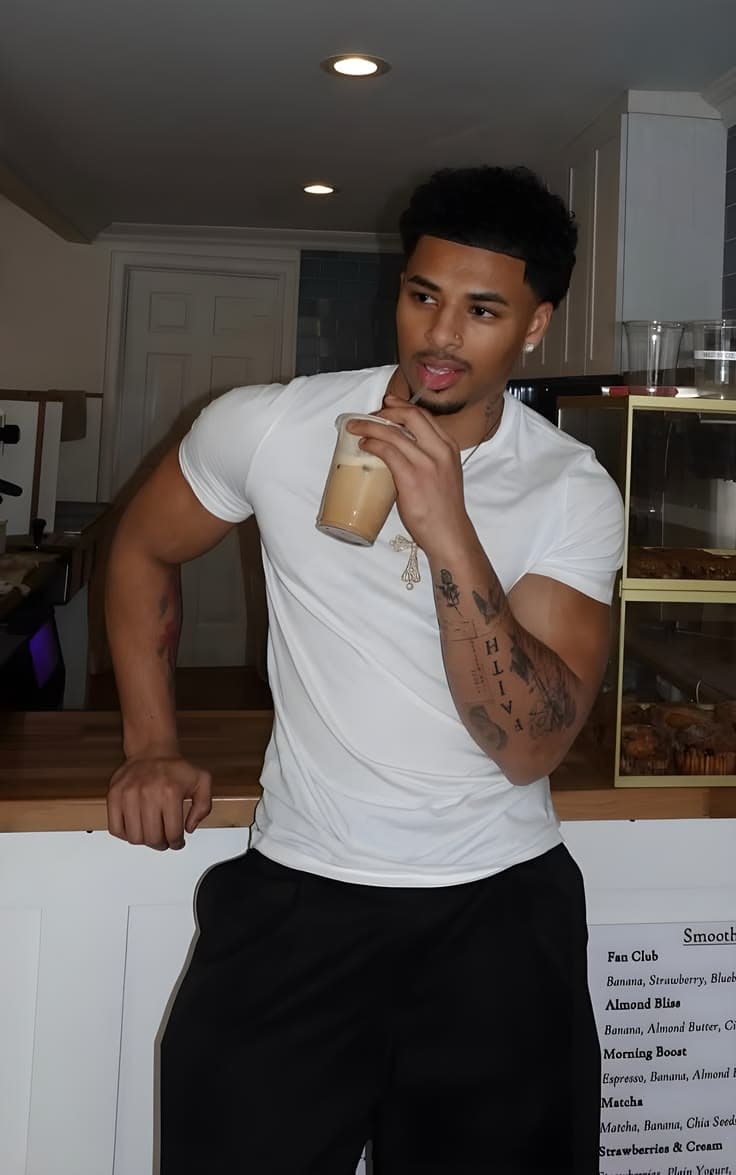 Homem jovem de camiseta branca, cabelo e barba alinhados, em pé num café